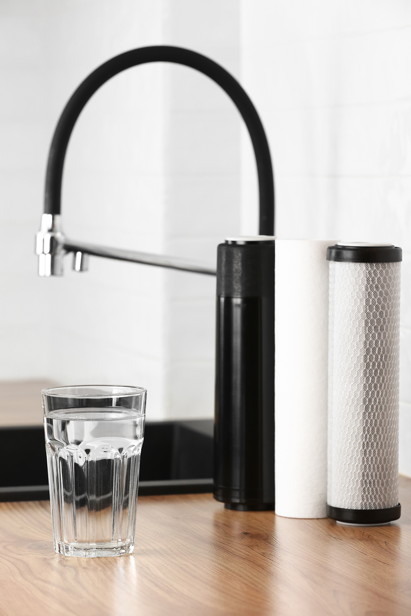 A glass of clean fresh water and set of filter cartridges on wooden table in a kitchen interior. Installation of reverse osmosis water purification system. Concept Household filtration system. House Water Filter
